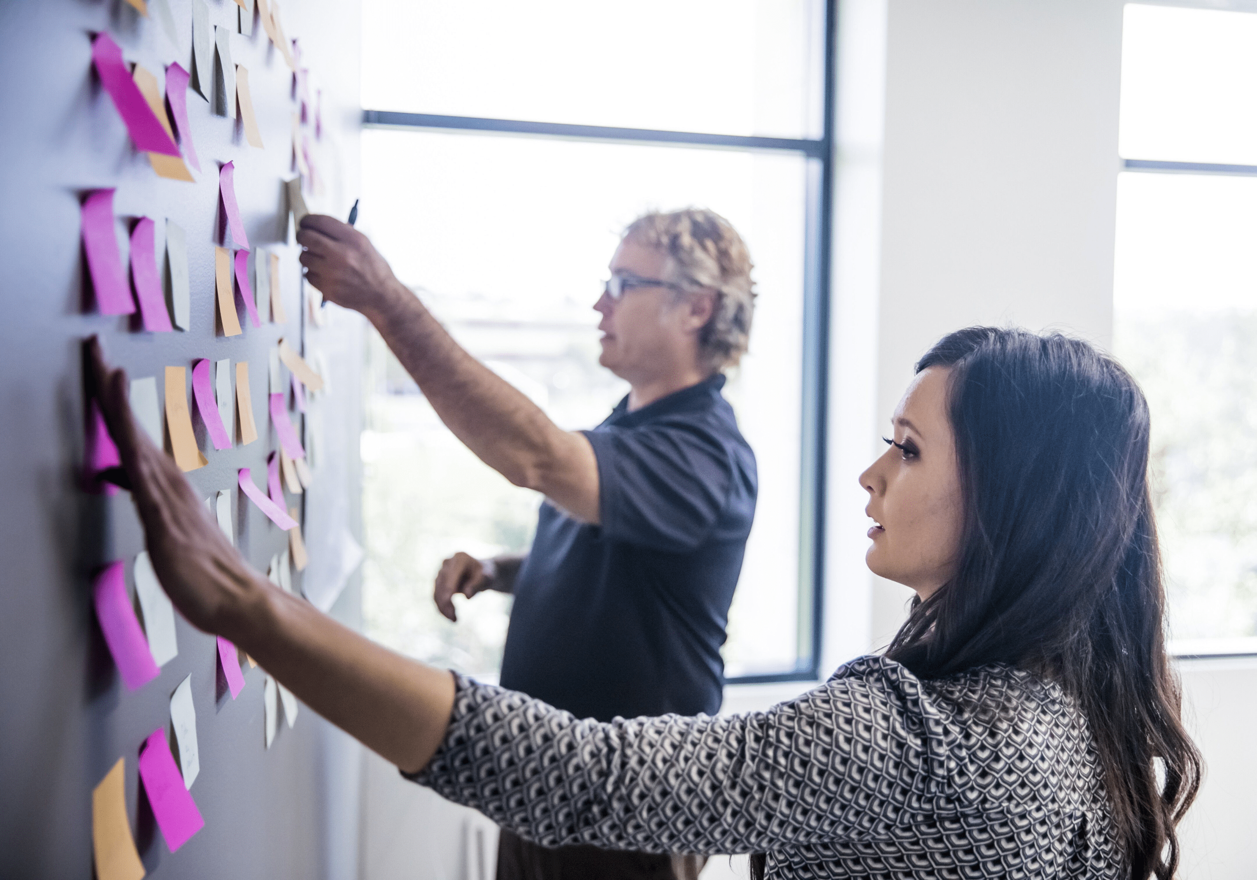 custom-solutions-two-colleagues-brainstorming-with-adhesive-notes-on-the-wall-original